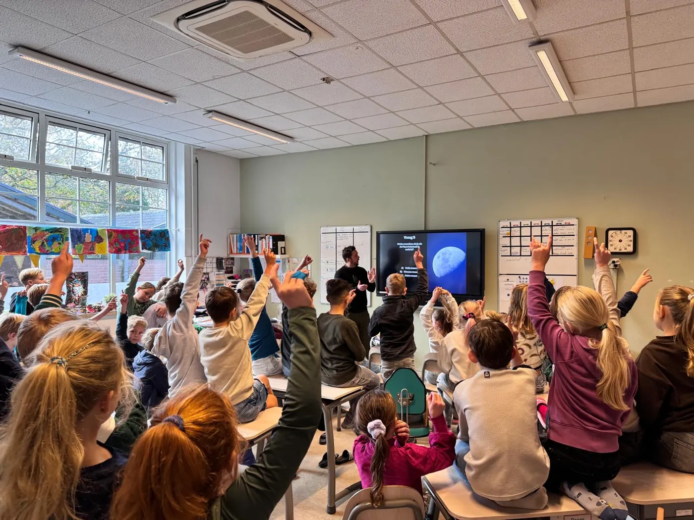 Een klas steekt massaal de vinger op bij een quizvraag over de maan